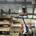 man on crane installing wiring into ceiling of warehouse