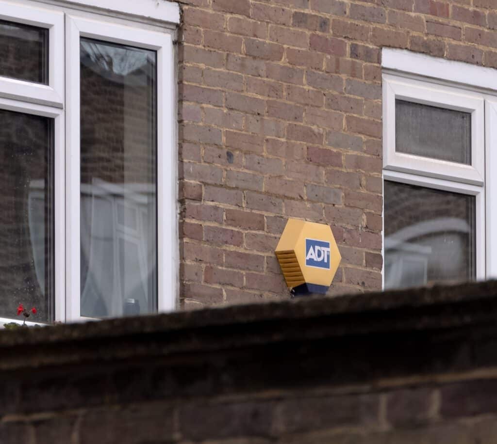 yellow and blue ADT burglar alarm mounted on wall of a house
